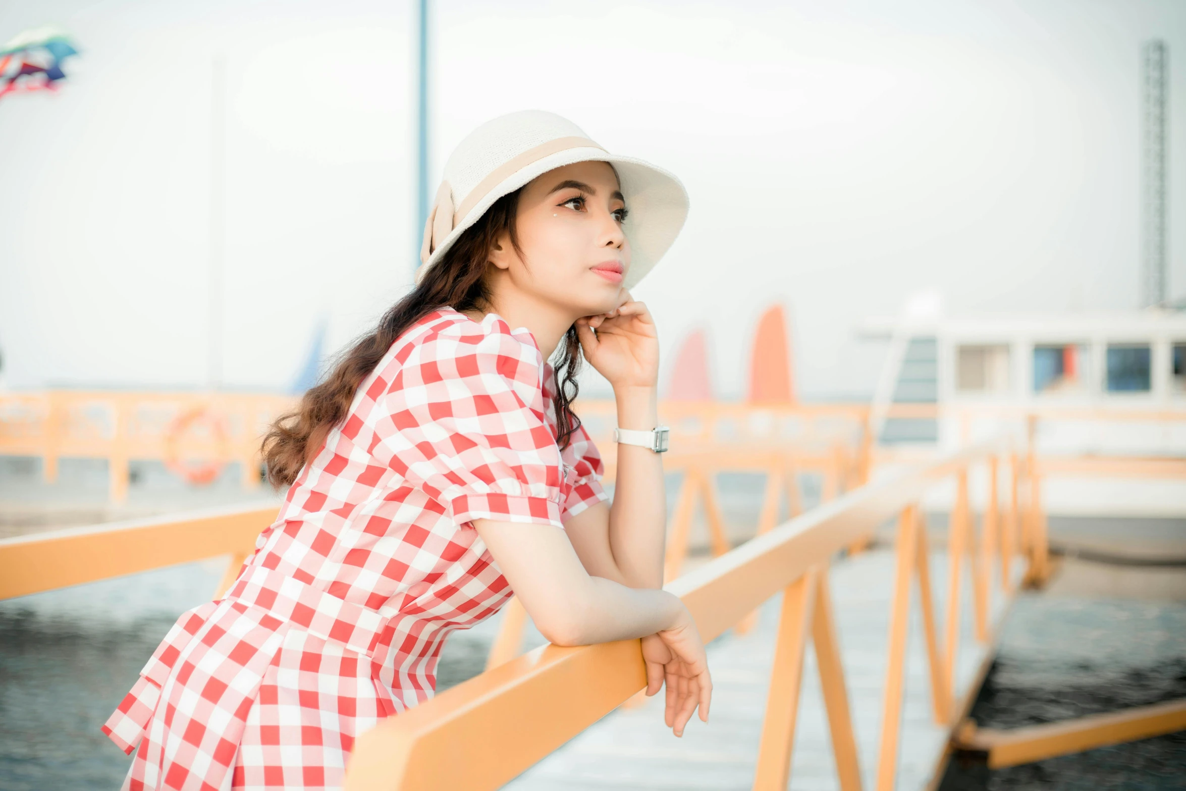 a woman in a red and white checkered dress leaning on a railing, by Ai-Mitsu, pexels contest winner, white straw flat brimmed hat, ulzzang, profile image, bright sky