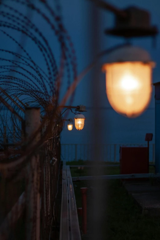 a light that is on top of a fence, a portrait, inspired by Elsa Bleda, unsplash, soviet yard, evening lanterns, seaview, low quality photo