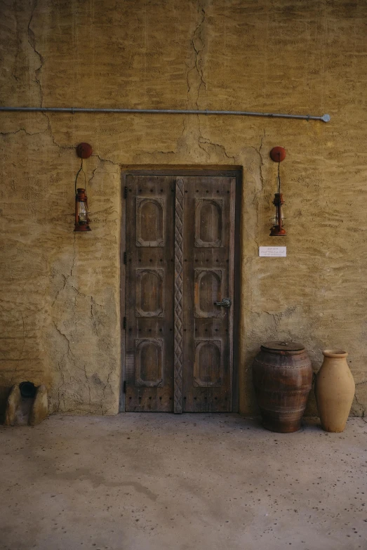 a door that is on the side of a building, inspired by Riad Beyrouti, barrels, light - brown wall, worn, on location