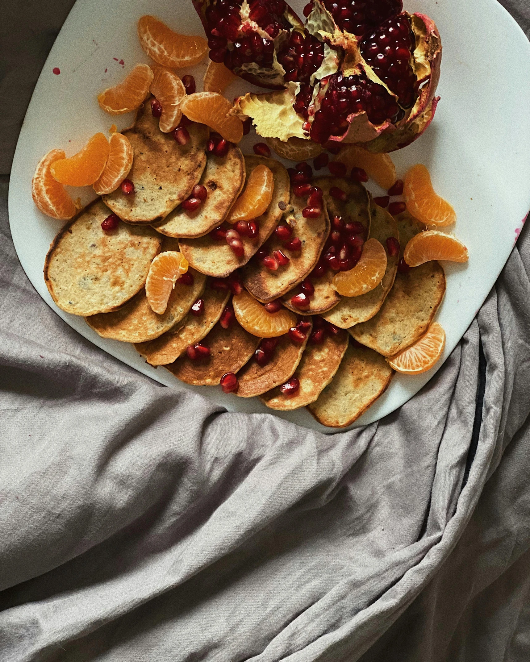 a white plate topped with orange slices and a pomegranate, by Alice Mason, pexels contest winner, loaves, on my bed, grey, full-body