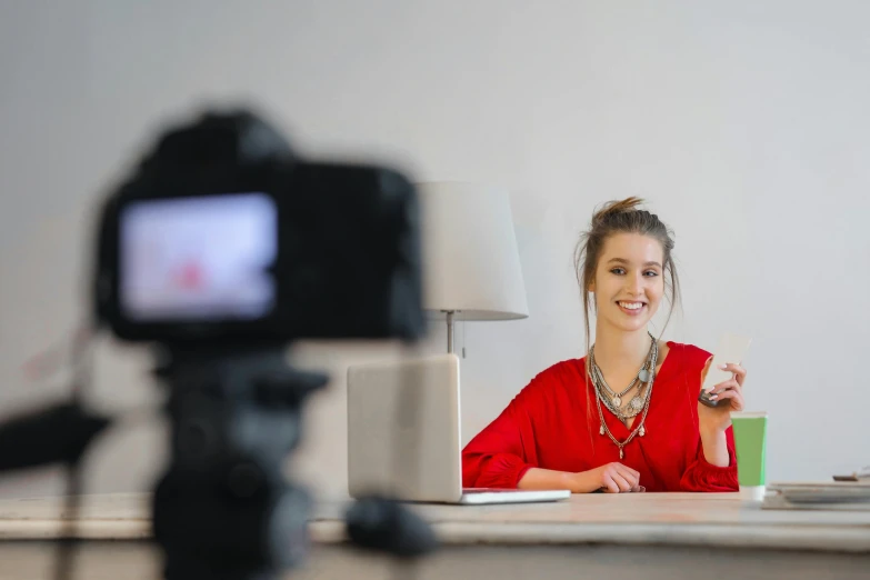 a woman sitting at a desk in front of a camera, trending on pexels, wearing a red outfit, avatar image, filmed, advertising photo