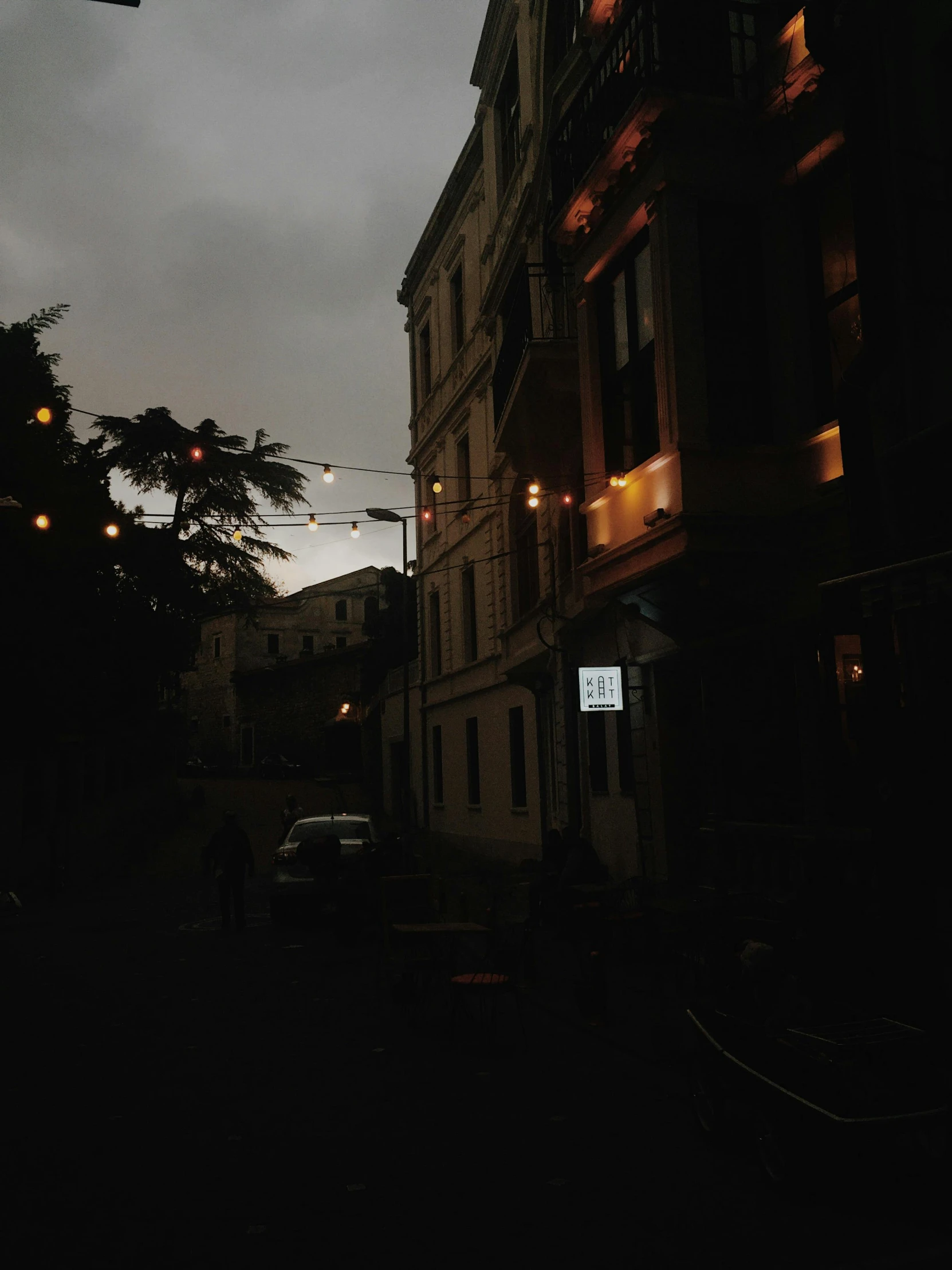 a street filled with lots of traffic next to tall buildings, an album cover, unsplash contest winner, renaissance, dimly-lit cozy tavern, overcast!!!, eerie and moody polaroid, evening lanterns