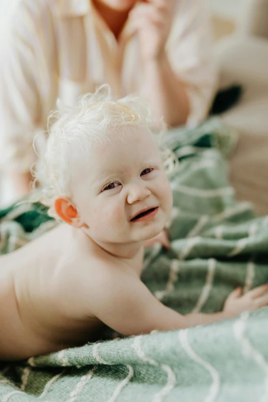 a woman sitting next to a baby on a bed, pexels contest winner, albino hair, closeup of an adorable, lachlan bailey, fluffy green belly