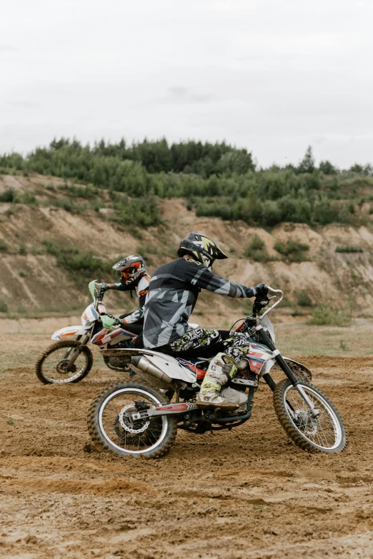 two people riding dirt bikes on a dirt track, unsplash, crazy detailed and complex, schools, grey, gold