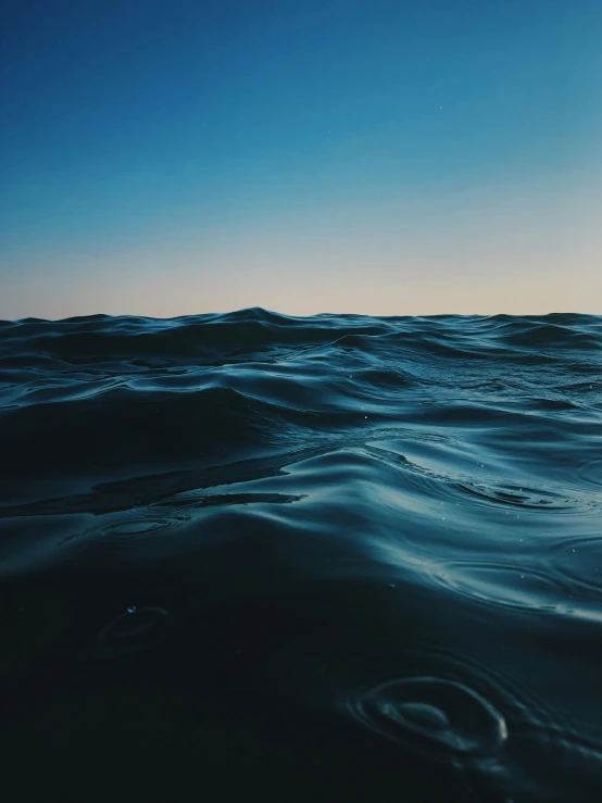 a large body of water under a blue sky, an album cover, by Ryan Pancoast, unsplash contest winner, dark ocean water, rippling electromagnetic, water levels, made of oil and water