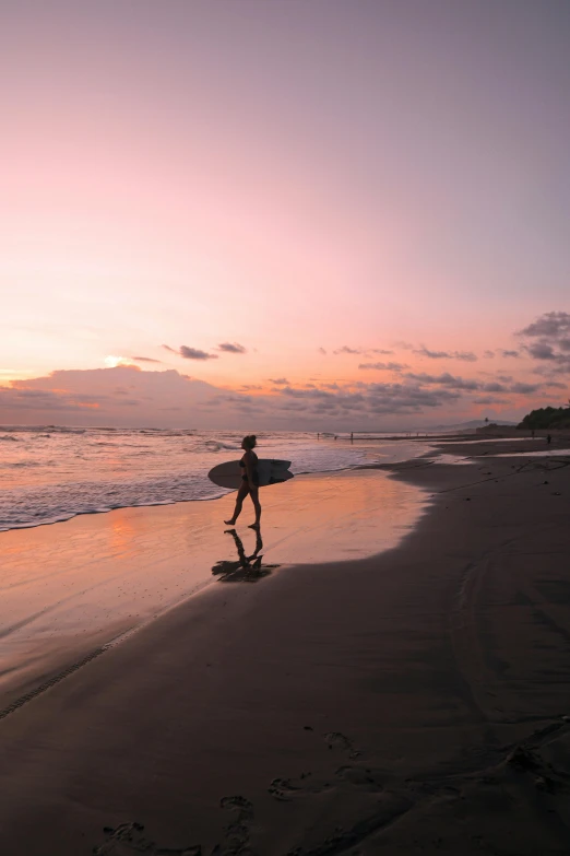 a person walking on a beach with a surfboard, during a sunset