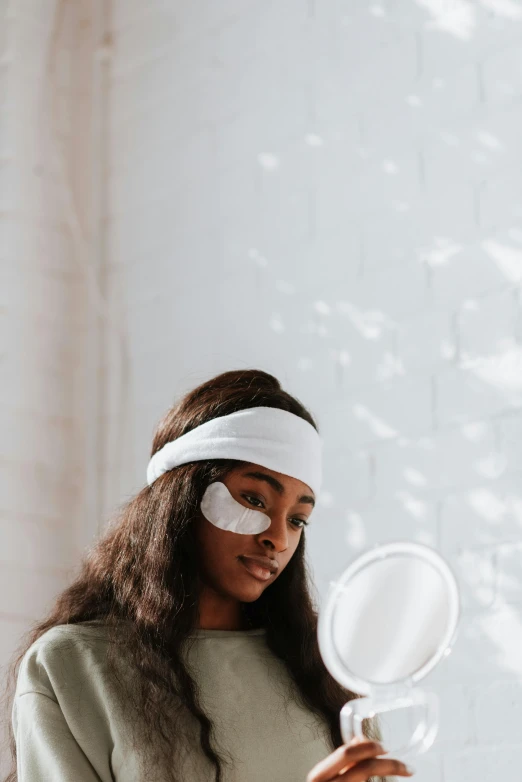 a woman holding a mirror in front of her face, trending on pexels, afrofuturism, black eye patch over left eye, wearing a headband, skincare, an all white human