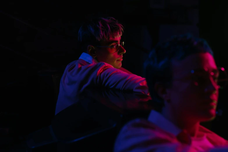 a couple of men sitting next to each other, by Nick Fudge, pexels contest winner, realism, barely lit warm violet red light, teenage boy, movie still 8 k, profile shot