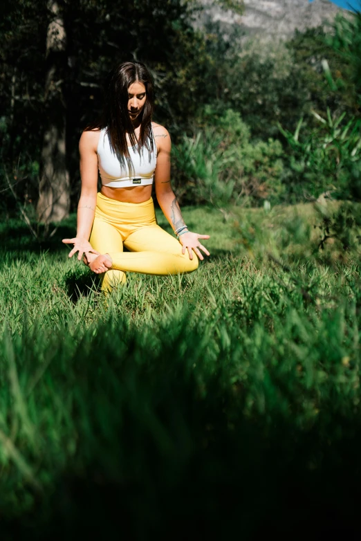 a woman sitting on top of a lush green field, wearing yellow croptop, figure meditating close shot, crouching, sydney hanson