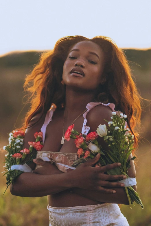 a woman standing in a field holding a bunch of flowers, an album cover, trending on unsplash, renaissance, rihanna, bralette, with brown skin, red haired goddess