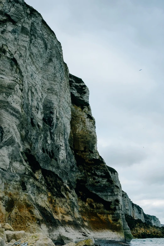 a man riding a surfboard on top of a sandy beach, a matte painting, unsplash, cliffs of dover, rock climbers climbing a rock, overcast skies, second eagle head