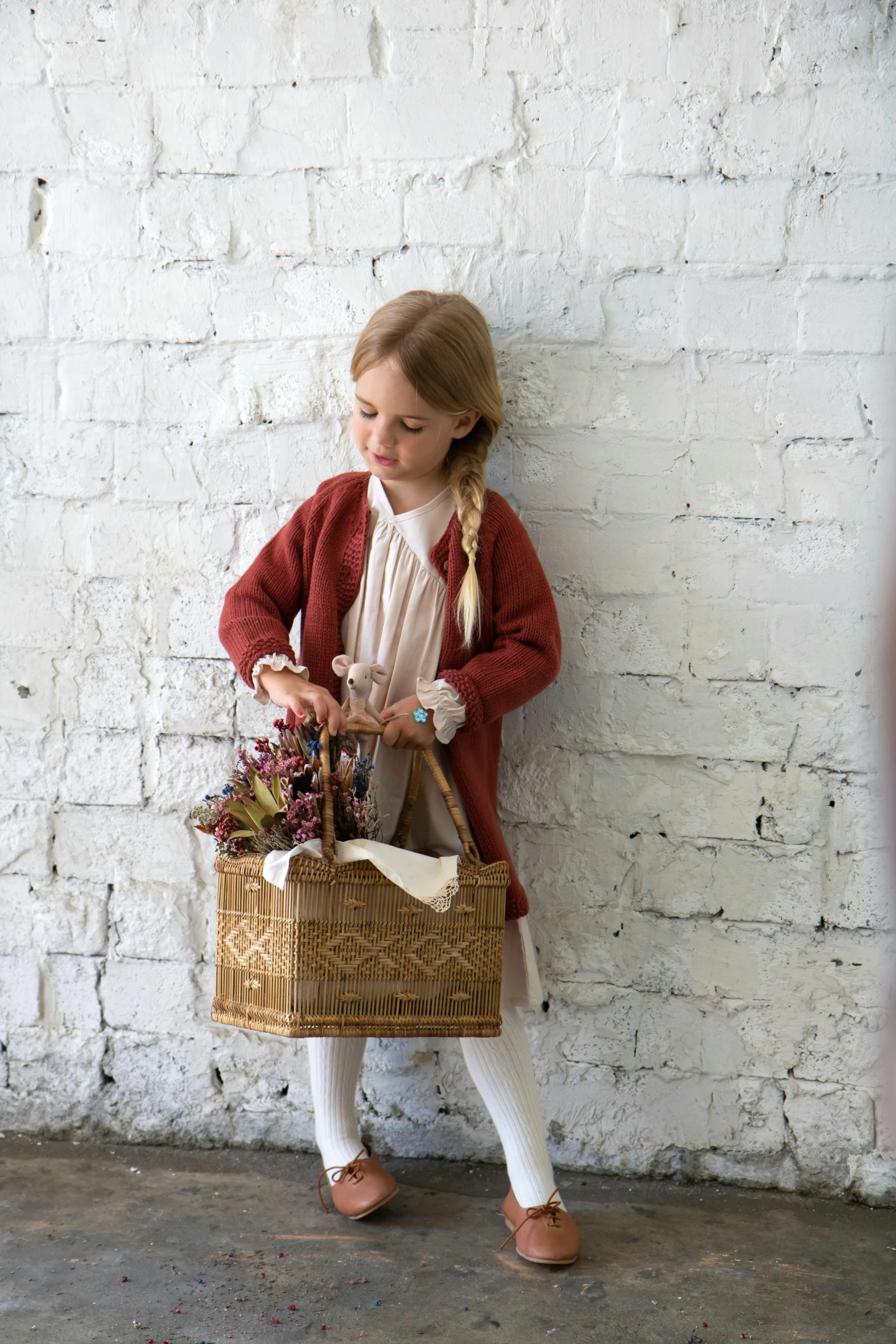 a little girl standing next to a brick wall holding a basket, inspired by Kate Greenaway, instagram, folk art, wearing a cardigan, product introduction photo, press shot, full product shot