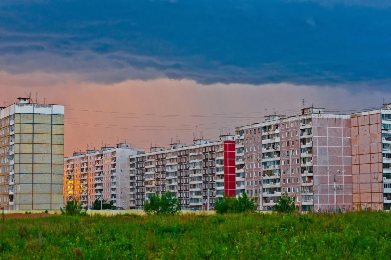 a group of tall buildings sitting on top of a lush green field, by Ihor Podolchak, pexels contest winner, socialist realism, red stormy sky, soviet suburbs, ten flats, today\'s featured photograph 4k