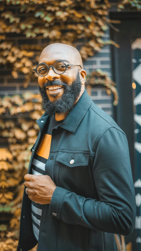 a man with a beard standing in front of a building, inspired by George Barret, Jr., pexels contest winner, large black smile, jamal campbell, man with glasses, headshot profile picture