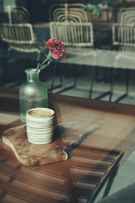 a cup of coffee sitting on top of a wooden table, a still life, inspired by Elsa Bleda, unsplash, vases and bottles, photo of a rose, restaurant, taken in the late 2000s