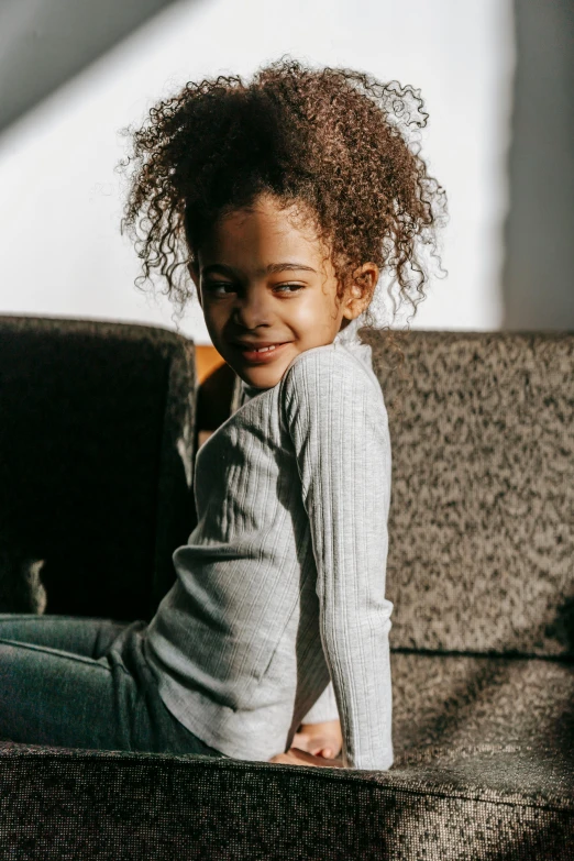 a little girl sitting on top of a couch, pexels contest winner, grey sweater, light-brown skin, ready to model, high - resolution