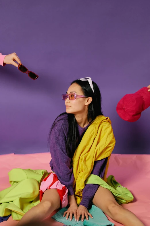 a woman sitting on top of a bed next to another woman, an album cover, inspired by Wang E, trending on pexels, purple outfit, neon sunglasses!, betty la fea, at a fashion shoot