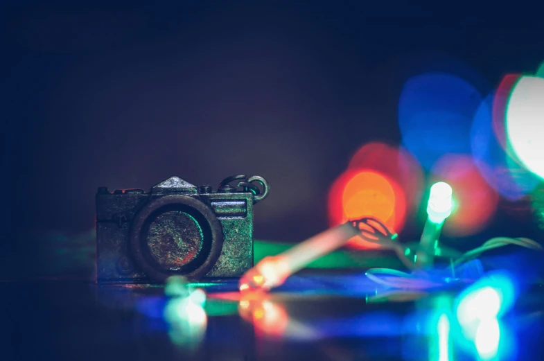 a camera sitting on top of a table next to christmas lights, by Adam Marczyński, art photography, multicoloured, multi - coloured, hasselblad film bokeh, miscellaneous objects