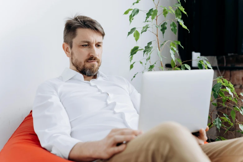 a man sitting on a bean bag chair using a laptop, by Adam Marczyński, trending on pexels, renaissance, wearing a white button up shirt, avatar image, serious, wearing business casual dress