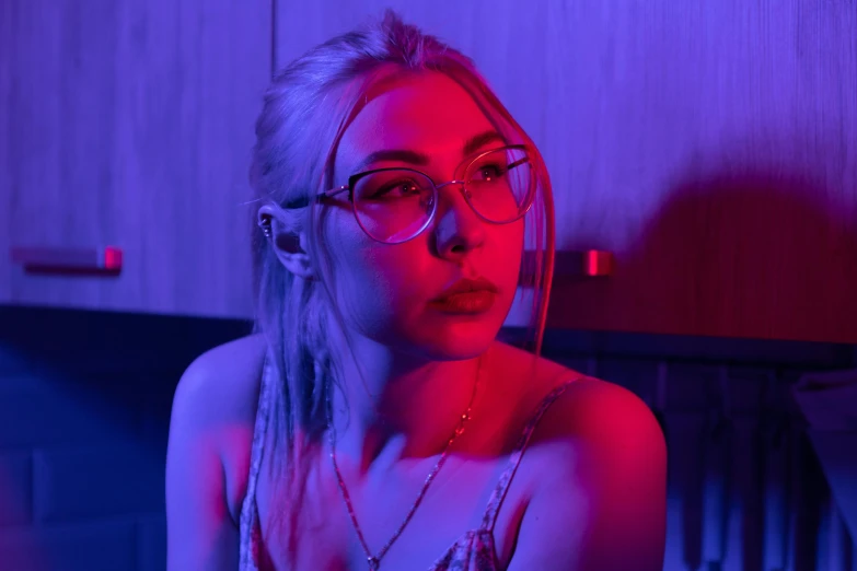 a woman with glasses sitting in a kitchen, an album cover, inspired by Elsa Bleda, trending on pexels, blue and red lights, young beautiful amouranth, purple neon, sydney sweeney