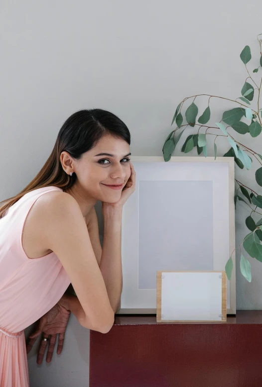 a woman in a pink dress leaning on a dresser, inspired by Juan Luna, pexels contest winner, square pictureframes, designed for cozy aesthetics!, smiling young woman, home display