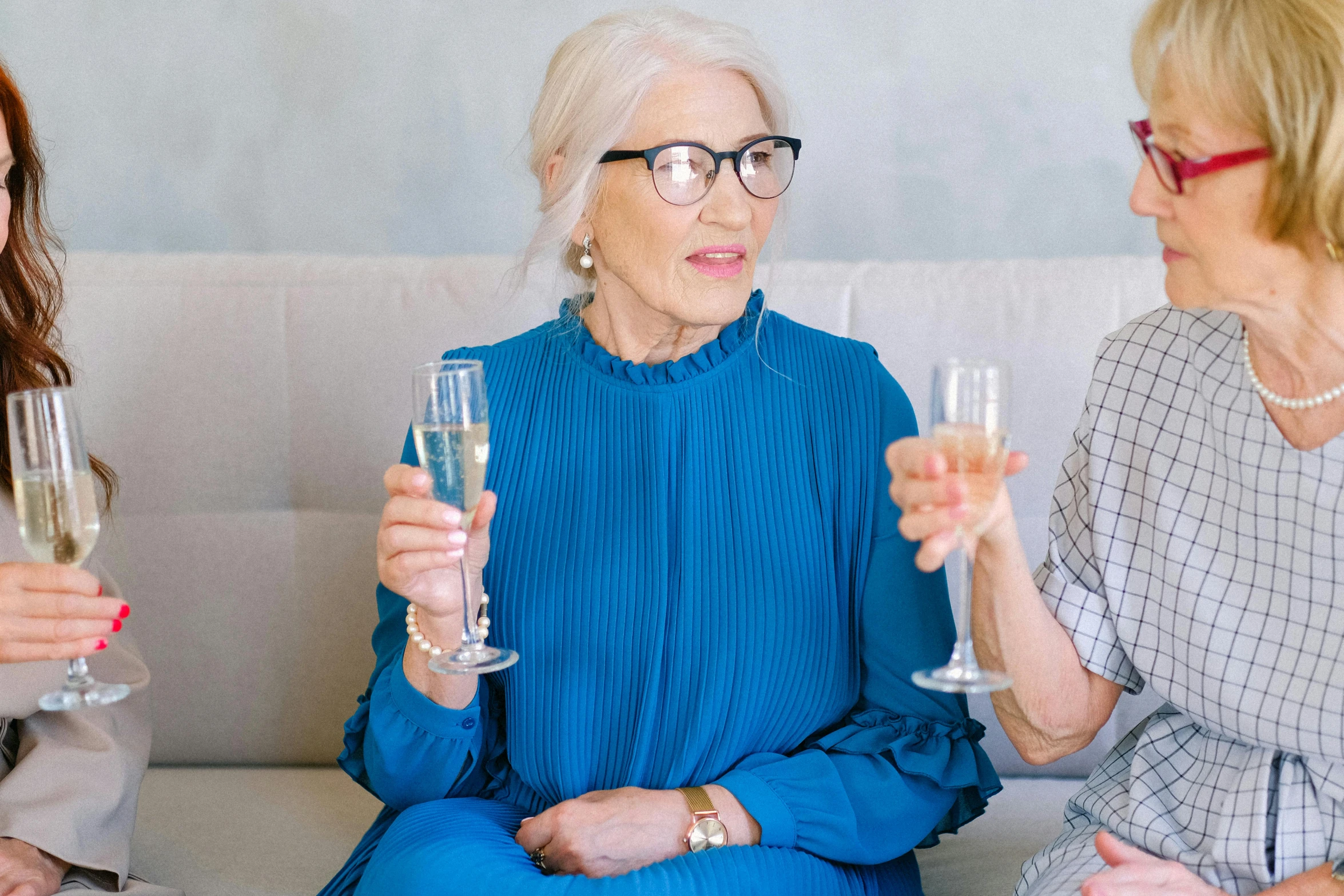 three women sitting on a couch holding wine glasses, pexels, white haired lady, square rimmed glasses, blue, drinking champagne