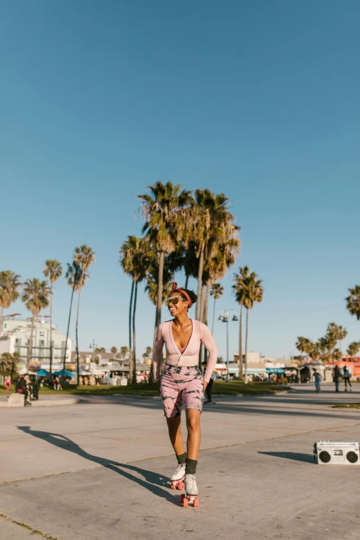 a woman riding a skateboard down a street next to palm trees, by Nina Hamnett, happening, boardwalk, wearing a colorful men's suit, bra and shorts streetwear, a person standing in front of a