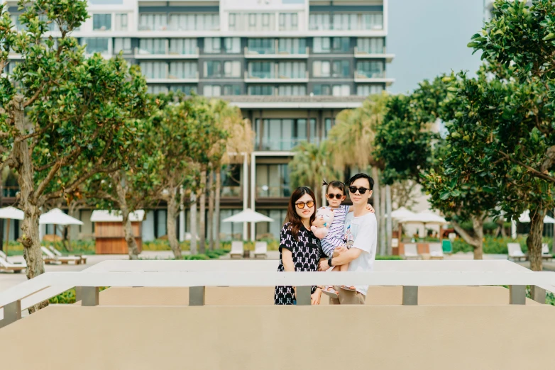 a family poses for a picture in front of a building, unsplash, minimalism, beach trees in the background, mixed development, gemma chen, parliament