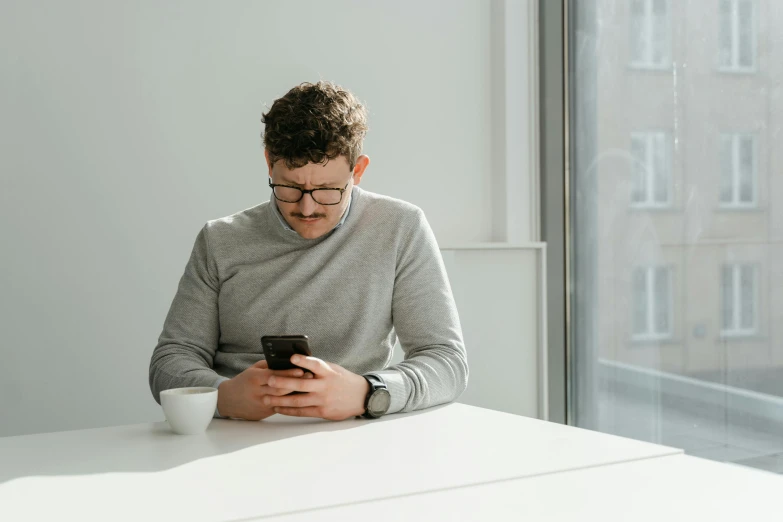 a man sitting at a table looking at his cell phone, trending on pexels, dressed in a gray, avatar image, kacper niepokolczycki, caucasian