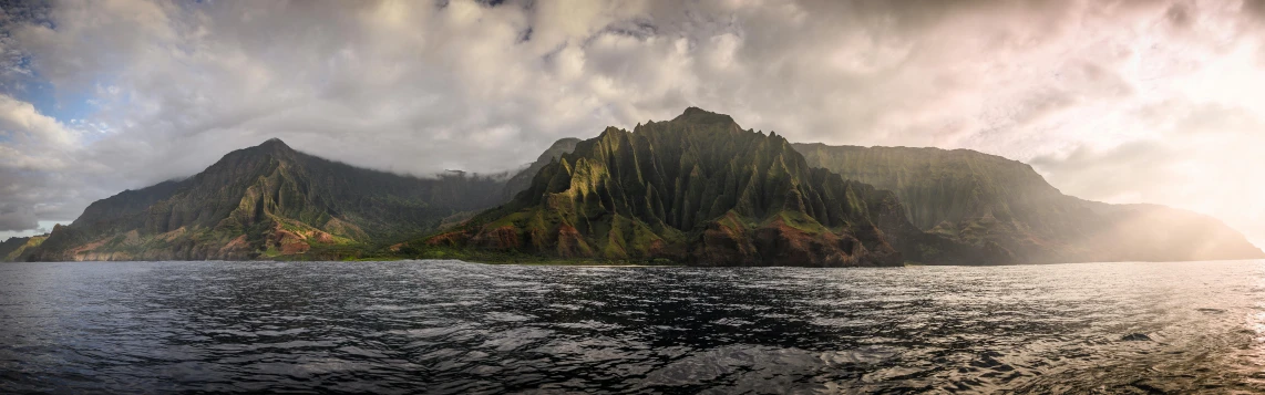 a body of water with mountains in the background, a matte painting, by Josh Bayer, pexels contest winner, hurufiyya, kauai, extreme panoramic, the photo was taken from a boat, coastal cliffs