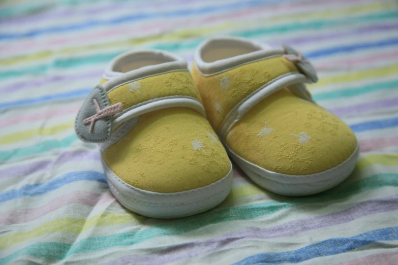 a pair of baby shoes sitting on top of a bed, yellow, small, clannad