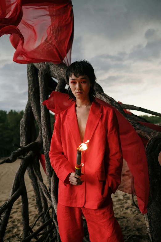 a man in a red suit standing next to a tree, an album cover, inspired by Taro Yamamoto, unsplash, gutai group, holding a candle, dragon-inspired cloth robes, an epic non - binary model, mei-ling zhou