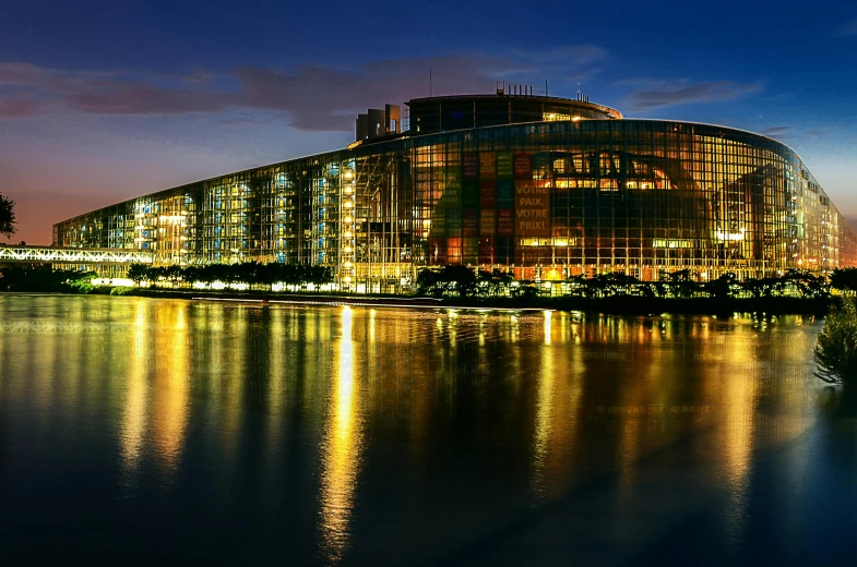 a large building sitting next to a body of water, by Michalis Oikonomou, pexels contest winner, european union, futuristic government chambers, in the evening, slide show