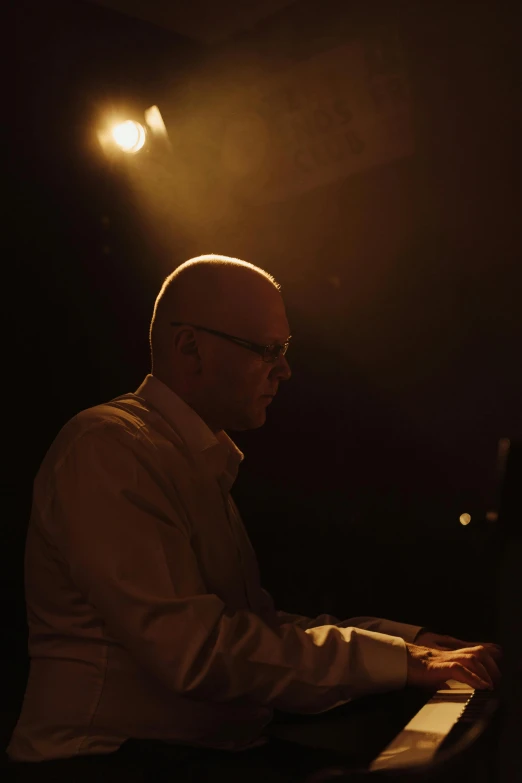 a man sitting at a piano in a dark room, by David Donaldson, philip selway (drums), taken at golden hour, performing, looking left