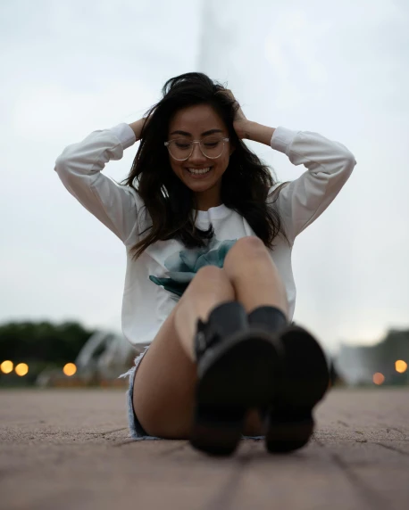a woman sitting on the ground in front of a fountain, pexels contest winner, tan skin a tee shirt and shorts, cute slightly nerdy smile, wearing a white sweater, trending on r/streetwear