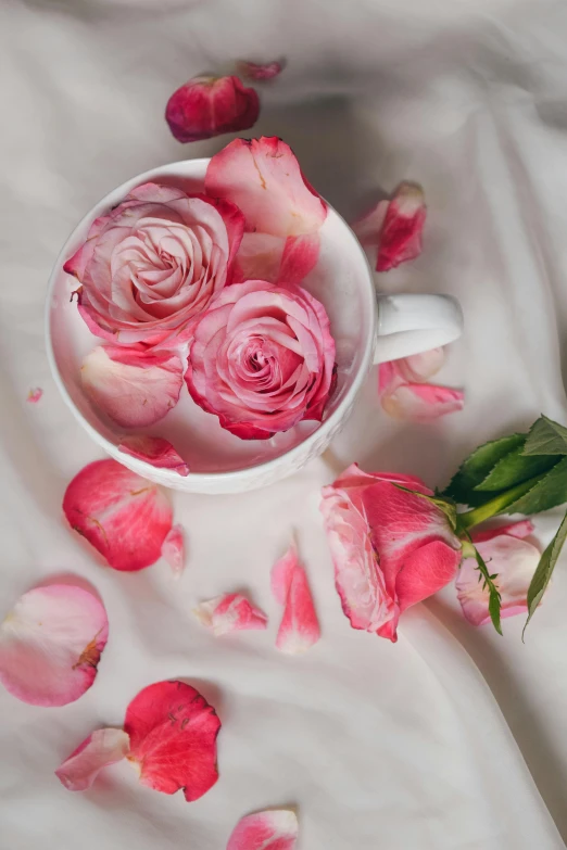 a white cup filled with pink roses on top of a bed, falling flower petals, botanicals, silk, zoomed in