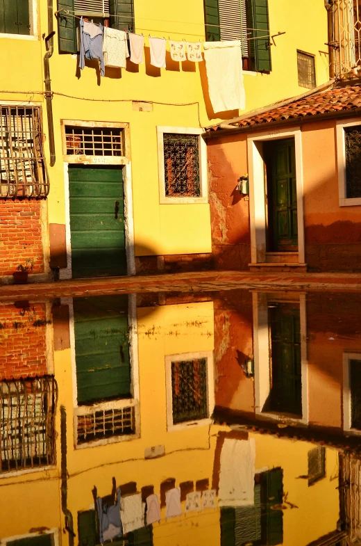 a reflection of a building in a puddle of water, flickr, sunlight and whimsical houses, venice, green and yellow, taken in the late 2010s