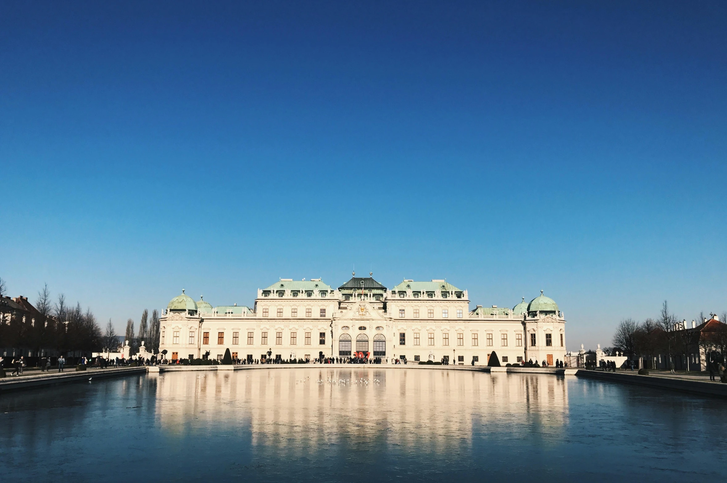 a large white building sitting next to a body of water, pexels contest winner, neoclassicism, vienna, blue sky, january, coronation