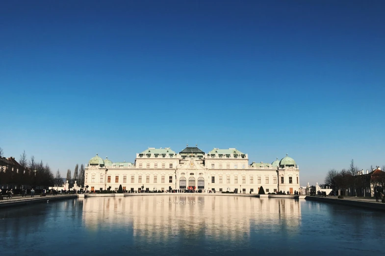 a large white building sitting next to a body of water, pexels contest winner, neoclassicism, vienna, blue sky, january, coronation