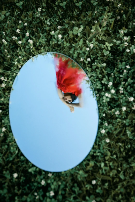 a mirror sitting on top of a lush green field, inspired by Scarlett Hooft Graafland, woman in flowers, fish eye lense, azure and red tones, looking down from above