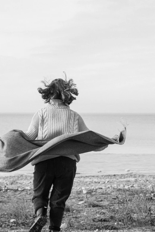 a black and white photo of a woman running on the beach, a black and white photo, inspired by Louis Stettner, pexels contest winner, conceptual art, covered with blanket, girl with feathers, overlooking, wearing a cardigan