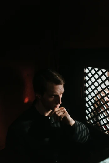 a man sitting at a table in front of a window, pexels contest winner, dark. studio lighting, in front of a carved screen, linus from linustechtips, holy lights
