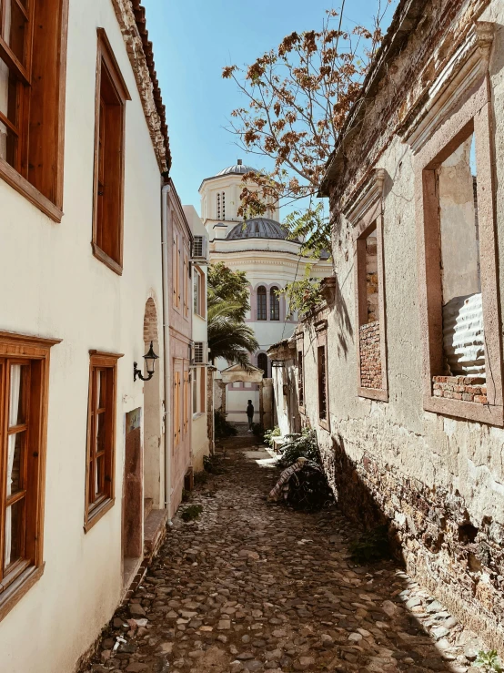 a narrow cobblestone street with a church in the background, greek architecture, profile image