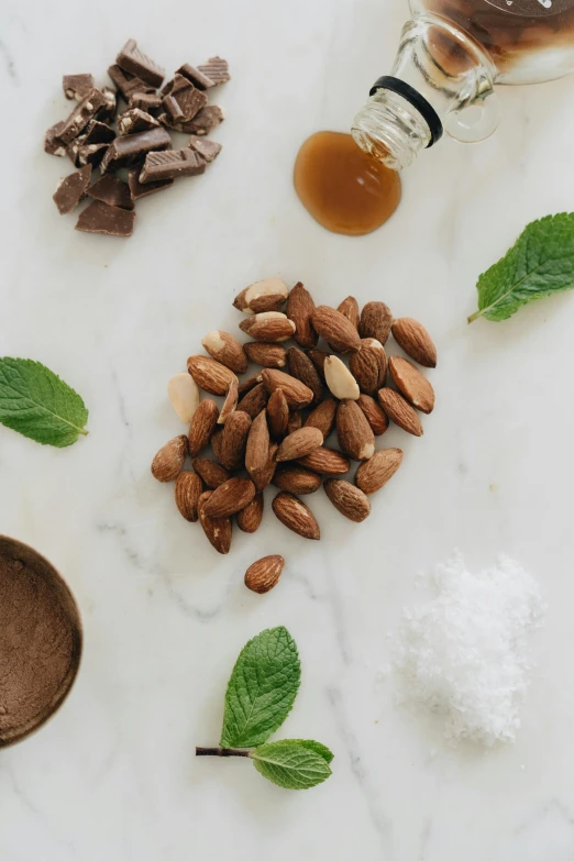 a white counter topped with nuts and chocolate, a still life, by Jessie Algie, trending on unsplash, mint leaves, brown almond-shaped eyes, detailed product photo, salt