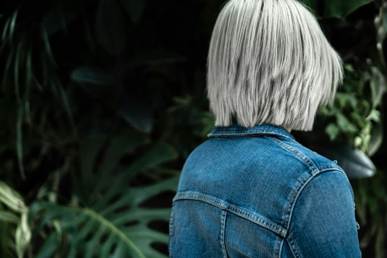 a close up of a person wearing a jean jacket, inspired by Elsa Bleda, trending on unsplash, silver hair so long, lush greenery, from the back, short bob hair
