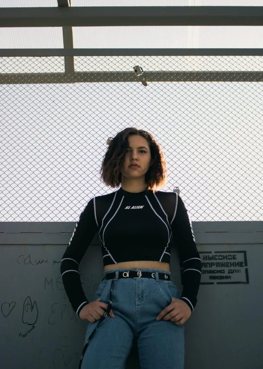 a woman leaning against a wall with her hands on her hips, an album cover, inspired by Elsa Bleda, unsplash, graffiti, (dark shorter curly hair), trending on r/streetwear, at future neon light rooftop, crop top