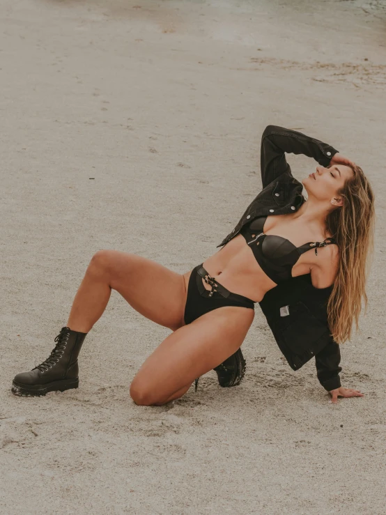 a beautiful woman laying on top of a sandy beach, by Robbie Trevino, dressed in biker leather, bra and shorts streetwear, profile image, squatting down next to a pool