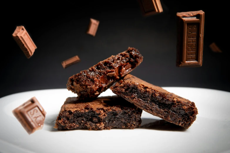 a white plate topped with brownies covered in chocolate, by Daniel Seghers, unsplash, bricks flying outwards, square, shot with sony alpha, eating mars bar candy