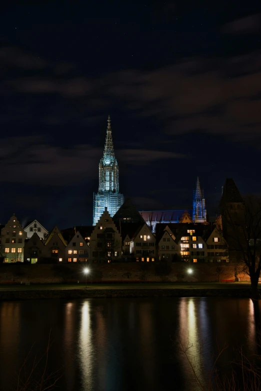 a city lit up at night next to a body of water, a picture, by Jan Tengnagel, pexels contest winner, renaissance, majestic spires, village in the background, high quality photo, taken with sony alpha 9