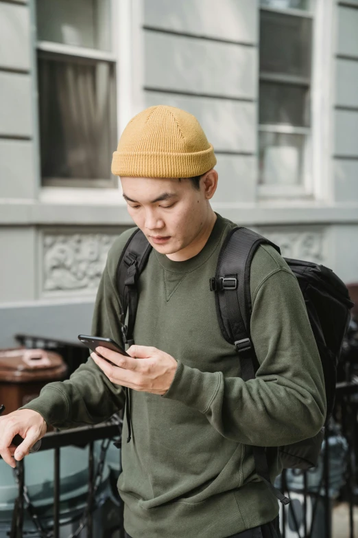 a man with a backpack looking at his cell phone, trending on pexels, wearing a beret, wlop and ross tran, yellow hue, university